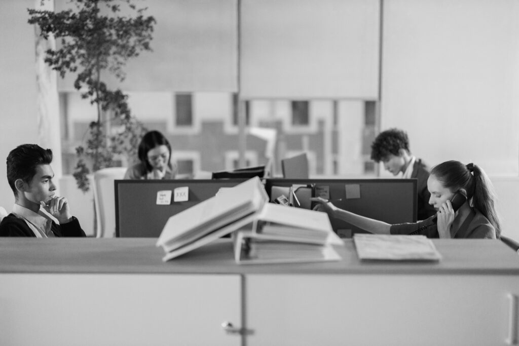Pracownicy siedzący w open space w biurze przy komputerach naprzeciwko siebie rozmawiający o dobrym adwokacie w szczecinku