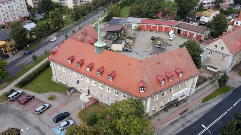 Budynek z lotu ptaka z dachem z czerwonej cegły z parkingiem przed. Budynek mieście się w mieście Szczecinek. W budynku znajduje się kancelaria, w której przyjmuje adwokat